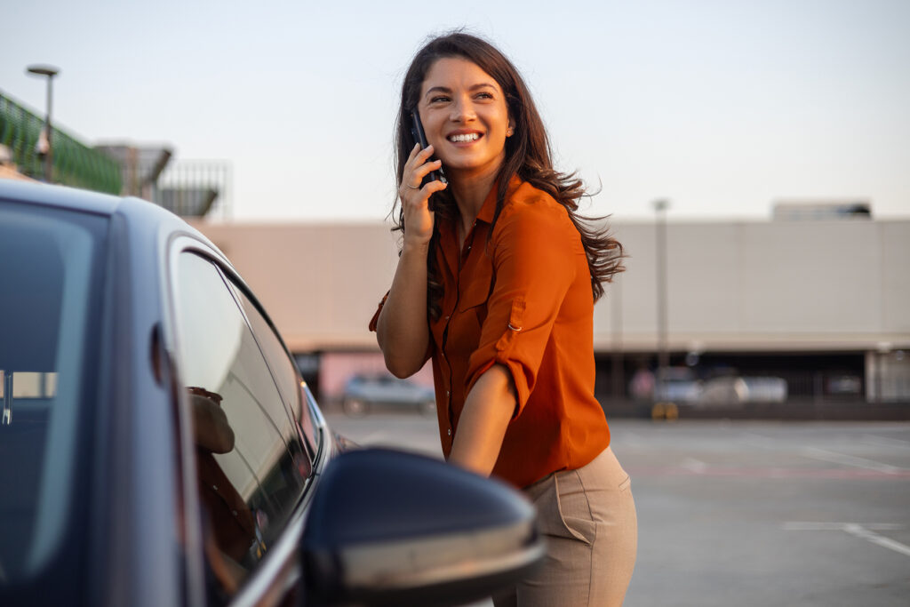 Woman on the phone, smiling, while unlocking her car
